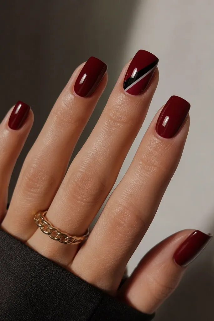 Square nails in glossy dark cherry red with a diagonal slash across the middle finger in black, plus a tiny white line parallel to it.