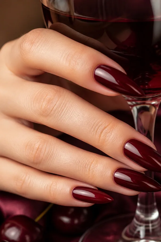 Close-up of dark cherry red stiletto nails with a high-shine mirror gloss. The nails are narrow with a sharp tip and clean, straight sidewalls. Light reflects as a smooth streak down the center of each nail.