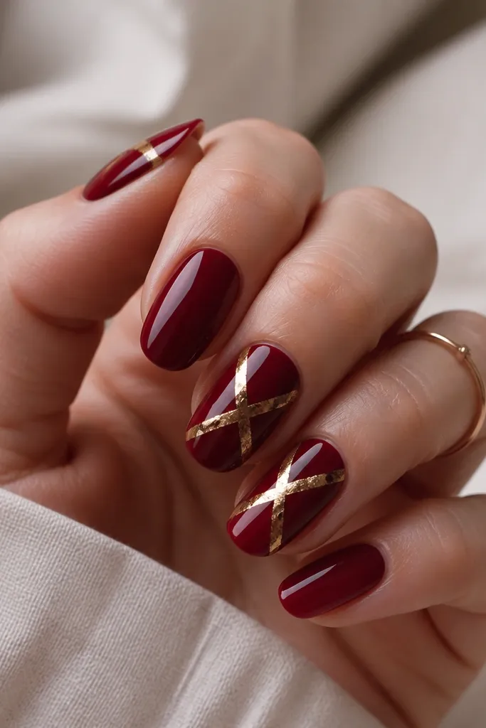 Dark cherry red nails with thin crisscross lines made from gold foil on two accent nails. The foil looks like torn strips forming an X pattern across the nail. Other nails are solid cherry red. Glossy top coat.