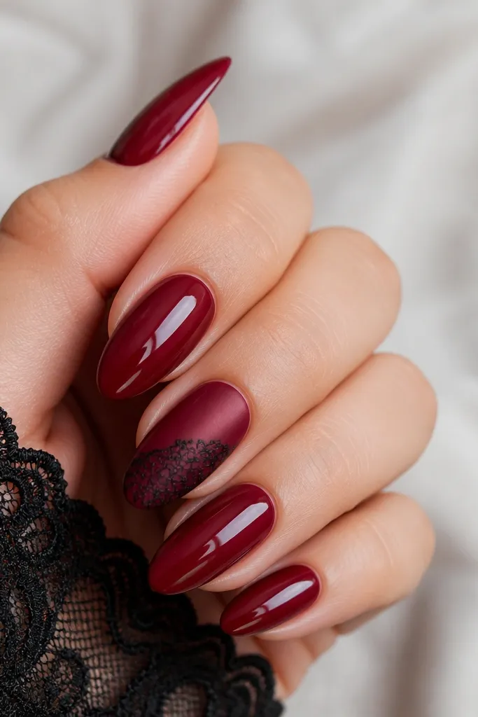 Dark cherry red nails with a lace pattern overlay on one accent nail. Lace is black with fine web-like lines and small loops, placed from mid-nail to near the tip. Other nails are solid cherry red. Matte top coat on the lace nail, glossy on others.