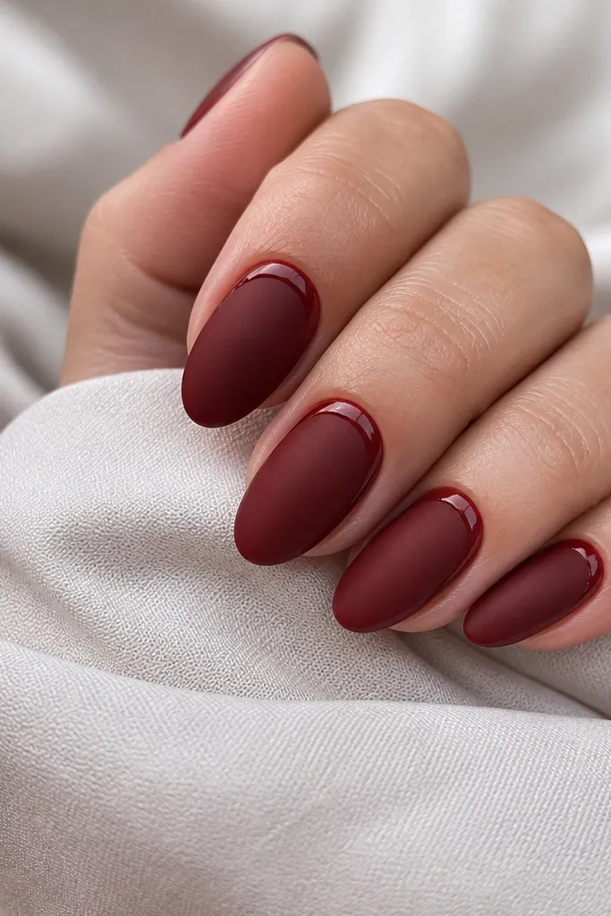Deep cherry nails with a velvety matte finish. Around the cuticle on each nail there is a thin glossy ring of the same cherry shade, creating a halo effect; nails are almond shaped.