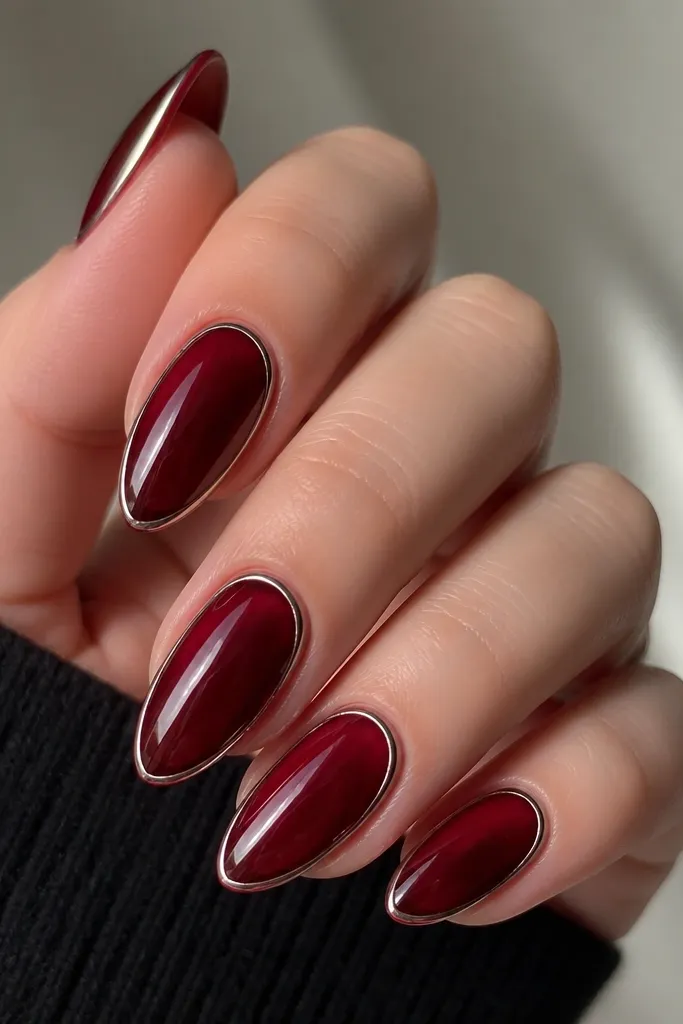 Translucent dark cherry nails with a glassy shine. A thin chrome strip runs along the outer edge of each nail, like a modern frame; almond shape, mirror-like edge.