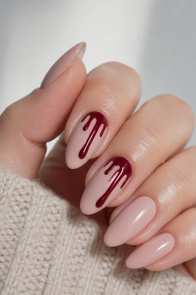 Nude pink nails with a dark cherry drip effect on two accent nails. The drips look like glossy paint running from near the cuticle down the center; other nails are solid nude glossy.