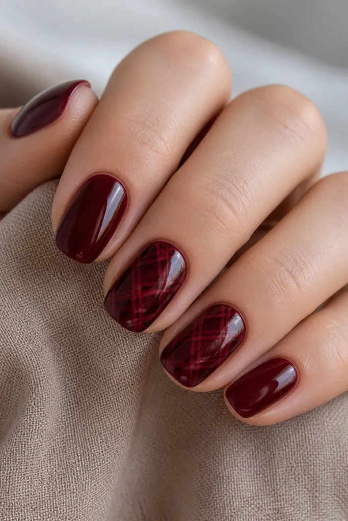 All nails are glossy dark cherry. Two nails have crisscross line art in a slightly lighter cherry and deep red, forming a lattice over the center; the lines are sharp and clean.