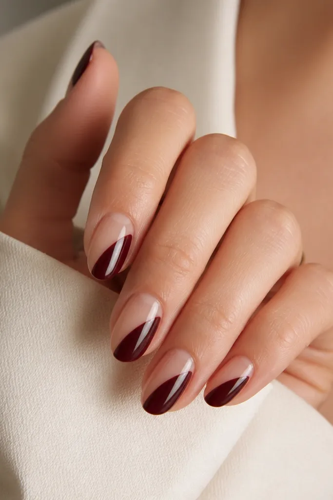 Clear nude nails with a glossy dark cherry half-glaze: one side of each nail is covered in dark cherry, leaving the other side sheer. There's a sharp diagonal boundary and mirror shine.