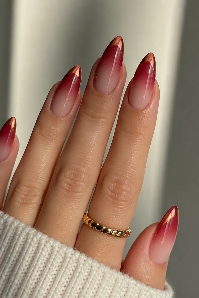 Almond nails with a cherry ombré fading into a soft nude base. The very tips have a red-gold shift chrome that flashes when you move your hand; glossy top coat.