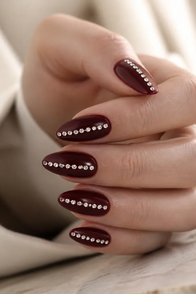 Glossy dark cherry nails with a single vertical rhinestone line running down the center of each nail. The stones are small, clear, and evenly spaced; nails are medium almond.