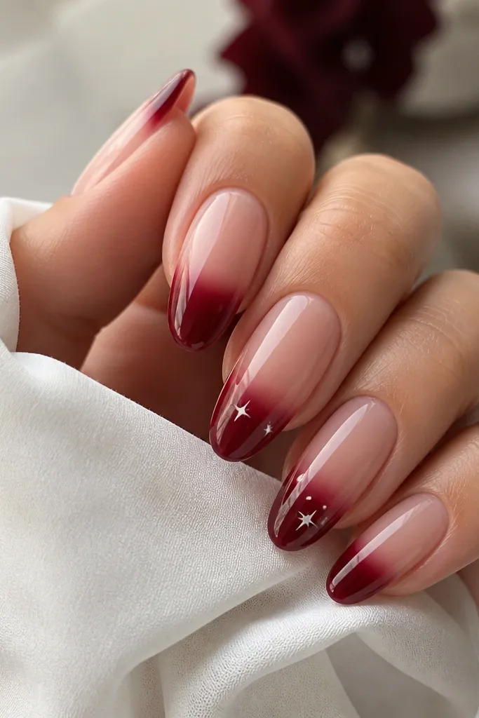 Nails have a clear pink base with dark cherry ombre at the tips. On two nails, tiny white star dots are placed near the ombre area; glossy finish.