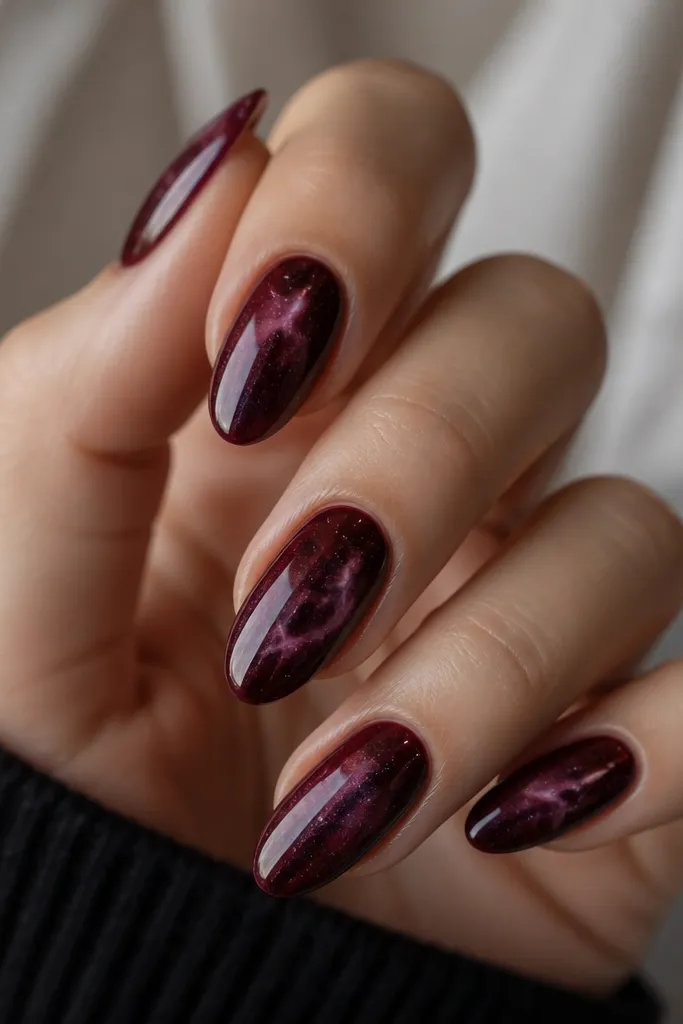 Dark cherry galaxy nails with swirling wisps of deep purple and tiny scattered dots. The nails are glossy and the pattern looks like space; medium almond shape.
