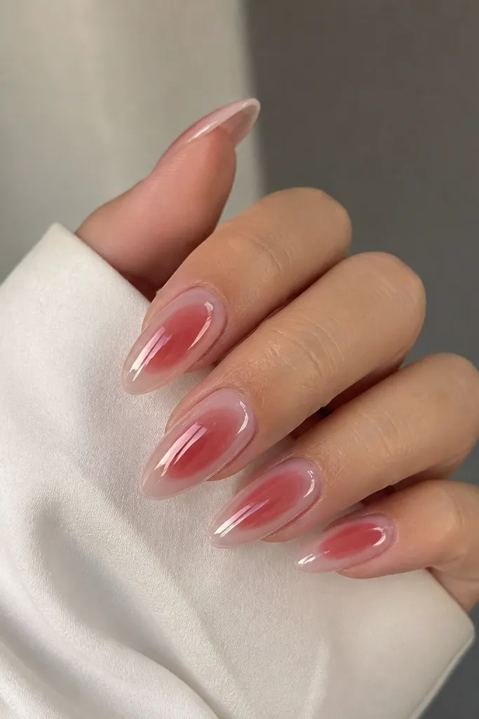 Clear pink nails with a soft dark cherry aura glow around the center. A faint chrome halo surrounds the glow, transitioning into a high-shine finish; almond shape.