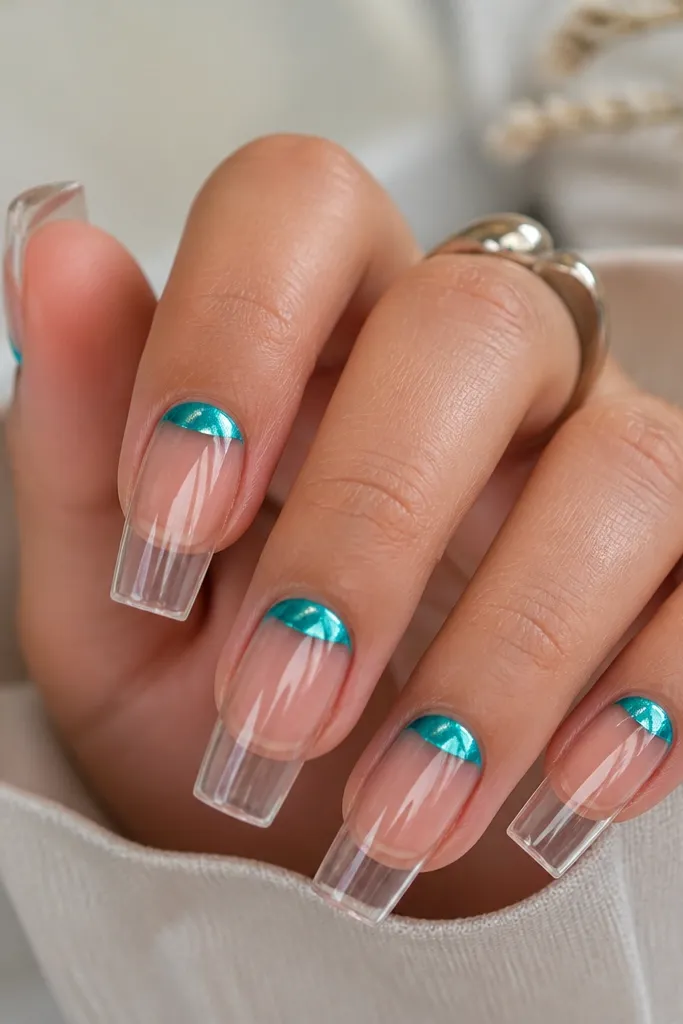 Long square nails with a clear base. A turquoise chrome half-moon sits just above the cuticle, centered and slightly curved across the nail width. The rest of the nail is transparent and glossy, with the chrome reflecting like a mirror.