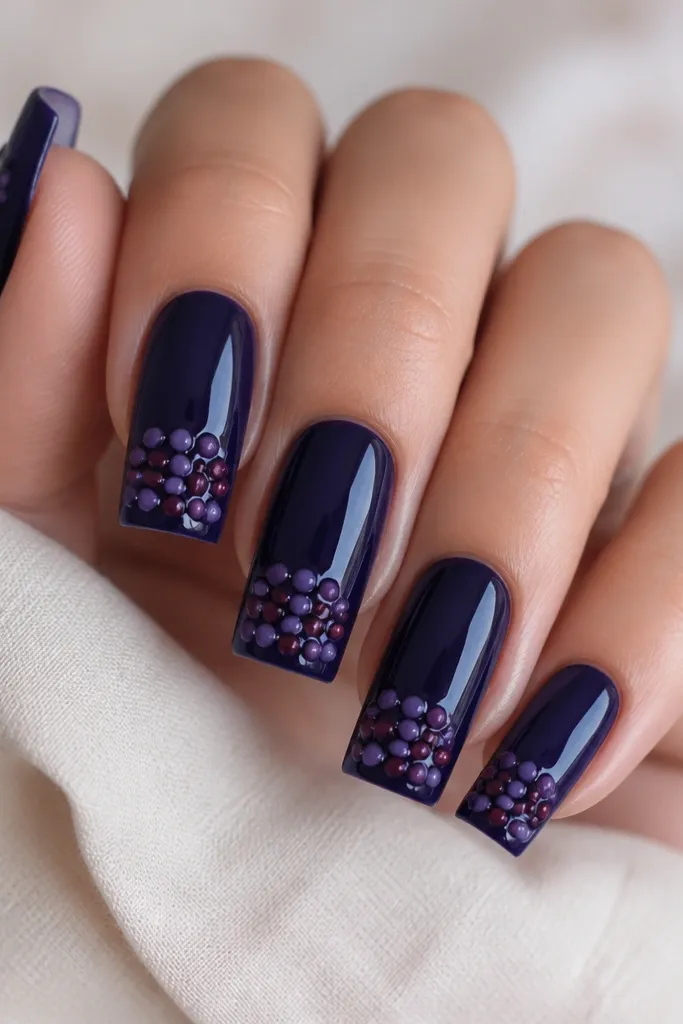 Long square nails in deep blueberry jelly. Near the tip, there's a cluster of raised glossy dot accents in purple and berry tones, shaped like tiny grape berries. The rest of the nail is smooth and glossy.