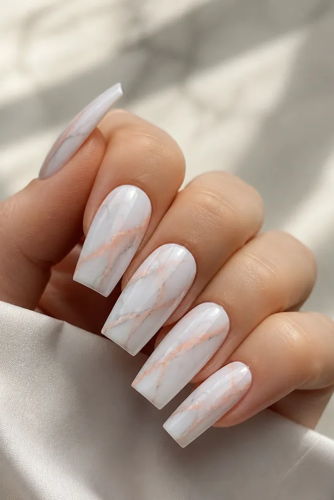 Long square nails with a milky white marble base. Thin peach veins run diagonally across each nail, with a few gray wisps for contrast. Surface is glossy, marble lines are sharp and clean.
