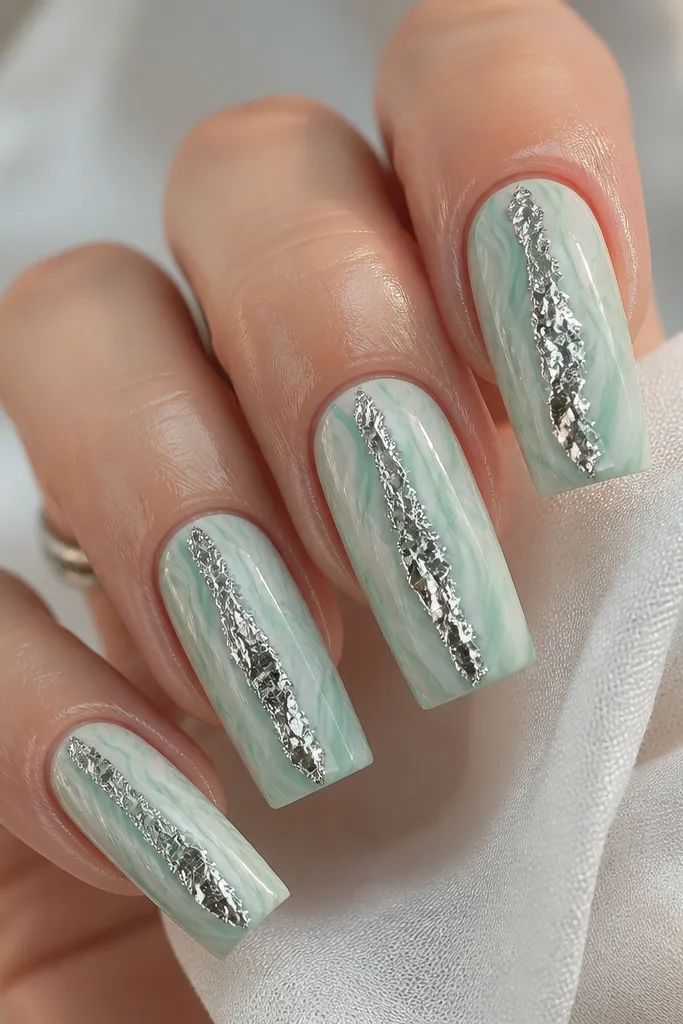 Long square nails with seafoam green marble swirls over a pale base. Along the center, there are irregular silver foil pieces that look like tears or droplets, slightly raised. Glossy and reflective.