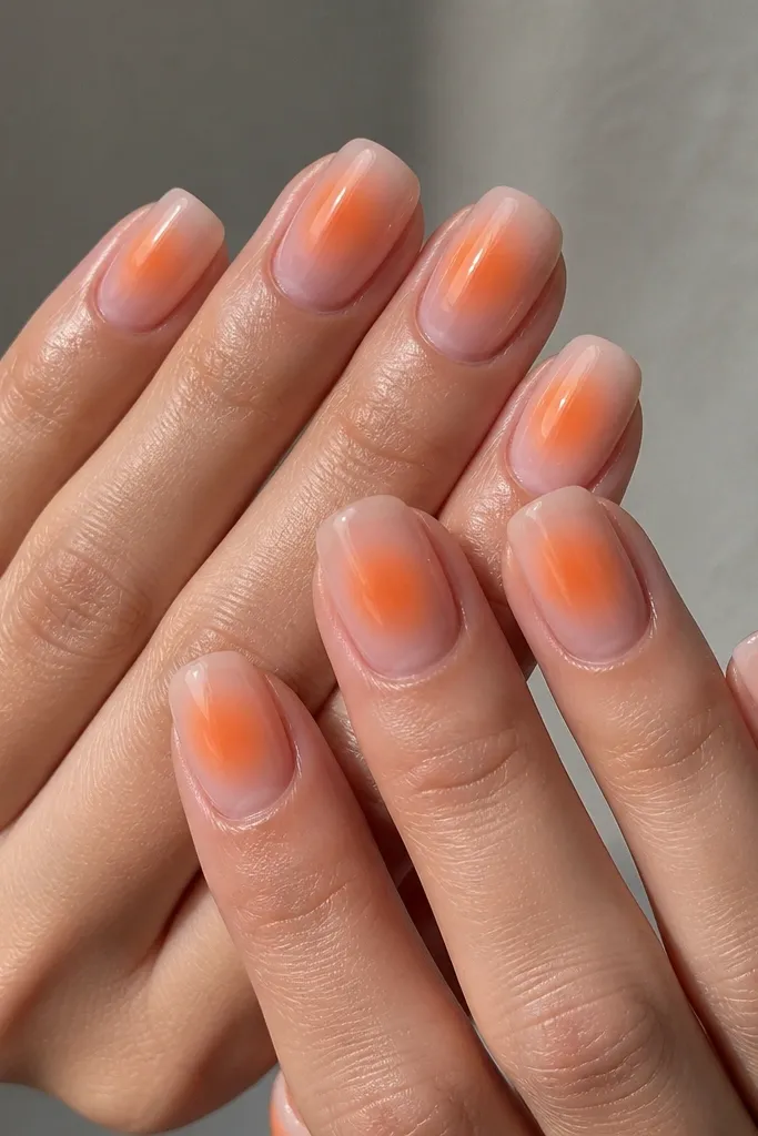 Square nails with a sheer nude base. A soft tangerine gradient sits around the center area like an aura, with a blurred glow and a glossy finish.