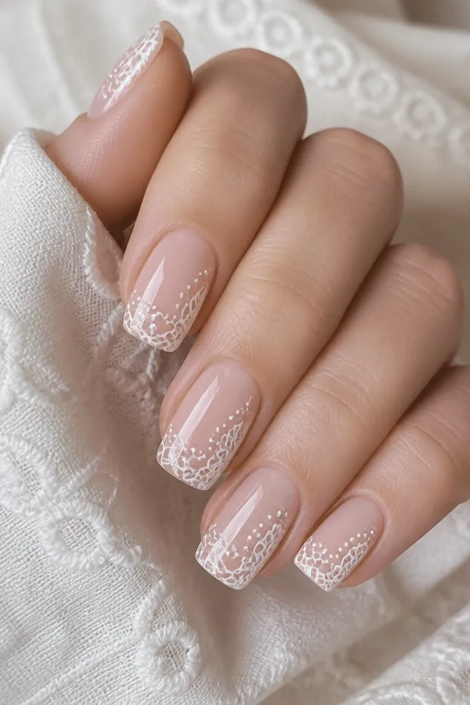 Square nails with a nude base. Thin white lace pattern appears like eyelet embroidery on each nail, with small loops and dots. The nails are glossy and the pattern is crisp.