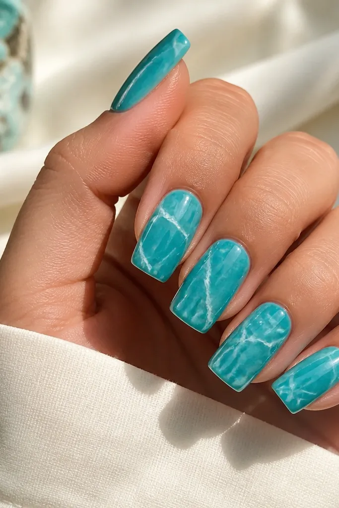 Square nails with turquoise base; irregular white marble veins spread across each nail, all under a glossy finish.