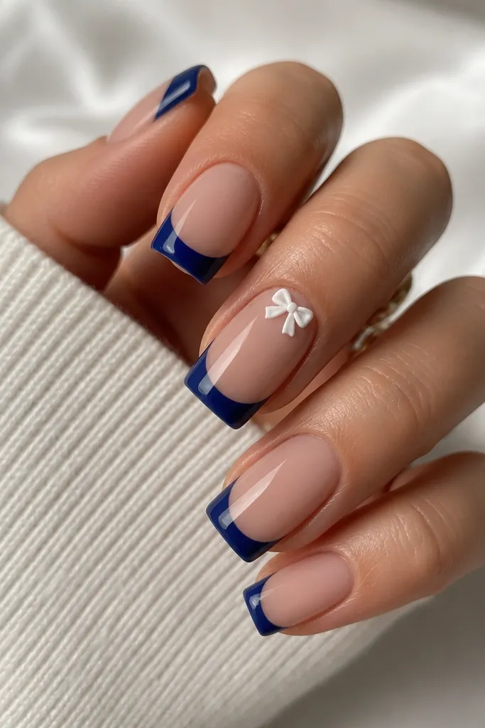 Square nails with nude base and deep blueberry French tips; on one nail, a tiny white bow tie sits near the cuticle, glossy.