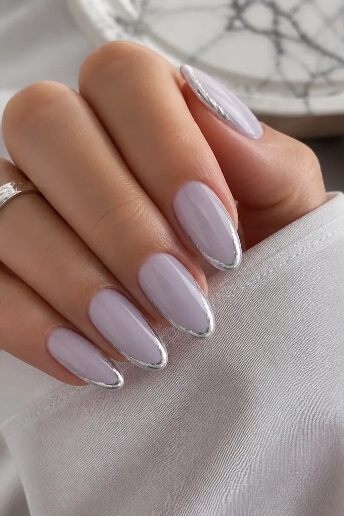 Almond nails in a lavender milky base with a thin silver foil strip along the outer edge of each nail. The foil is irregular but controlled and glossy.
