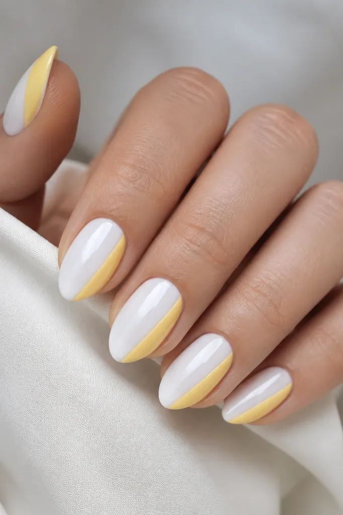 Glossy white almond nails with a buttery yellow half tip that covers the outer half of the free edge, leaving the inner half white.
