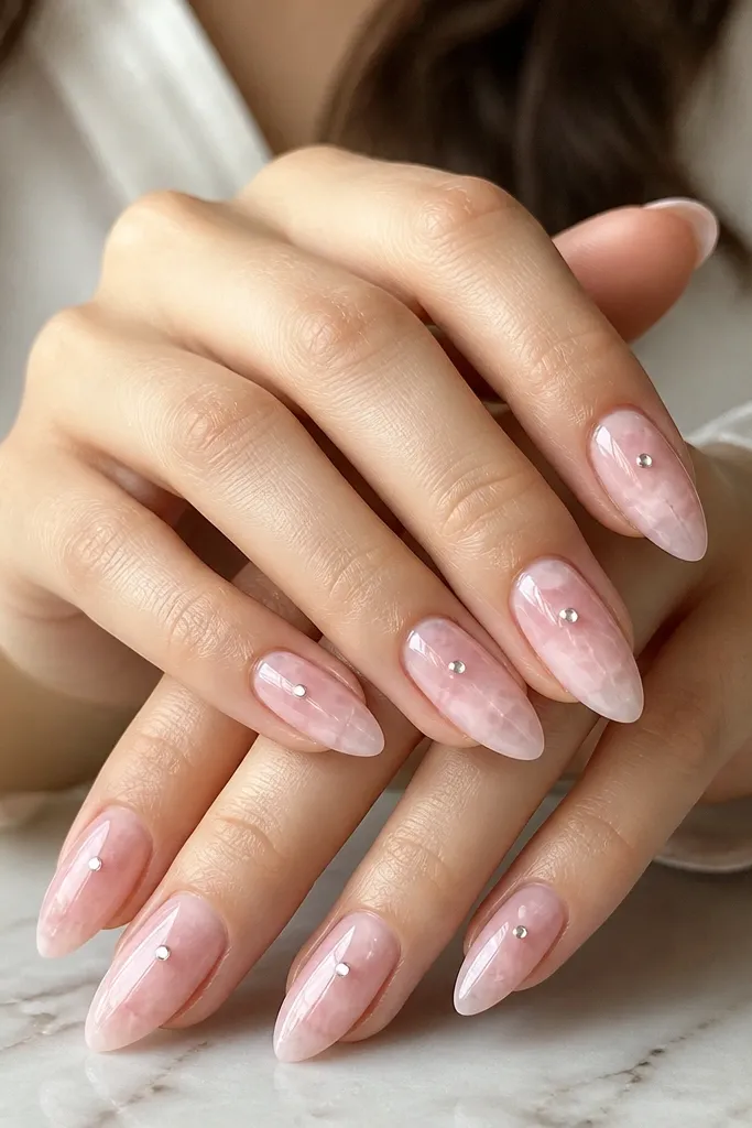 Almond nails with a pink rose-quartz marbled base and one clear gem dot near the center on each nail. The overall finish is glossy.