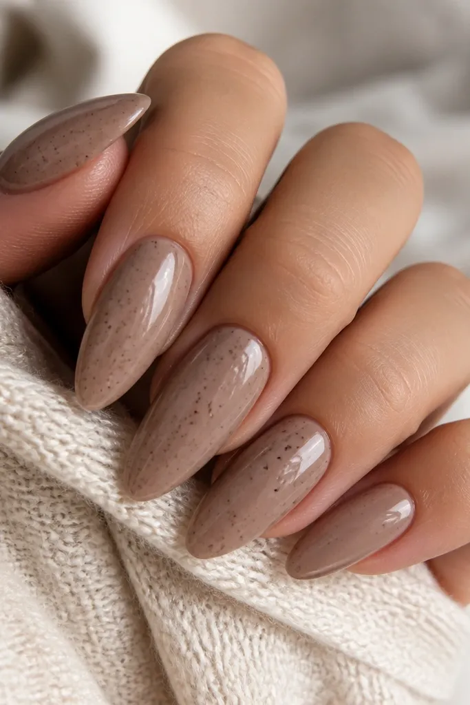 Almond nails in a mocha nude glossy finish with tiny espresso-brown speckles scattered lightly across the nail.
