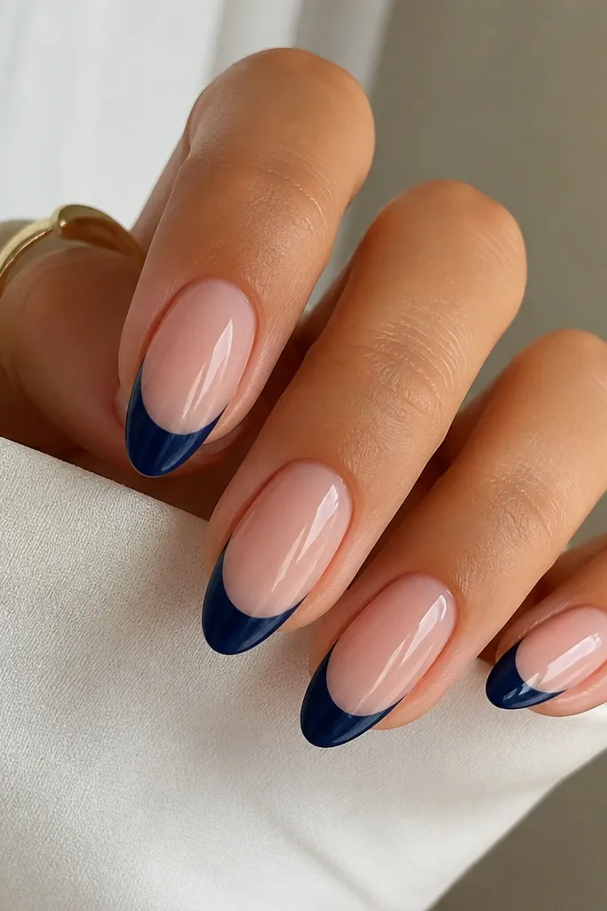 Medium-length almond nails with a sheer pink base. The tips are classic French in denim navy blue, forming a smooth curved white-French-like smile line. Everything is glossy and evenly centered on each nail.