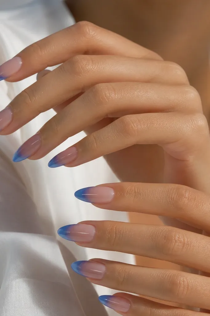 Long almond nails with a clear or barely-there base. The French tip starts royal blue at the center and fades to transparent toward the outer edge, creating a smooth gradient. Glossy finish, no glitter.