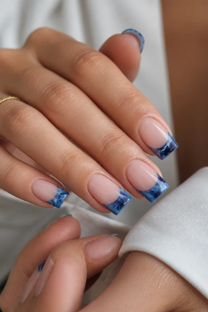 Square nails with a clear gel base. The French tips are blue marble pieces - swirls of navy, medium blue, and lighter blue with thin white veining. Glossy finish, each nail has a slightly different marble pattern.