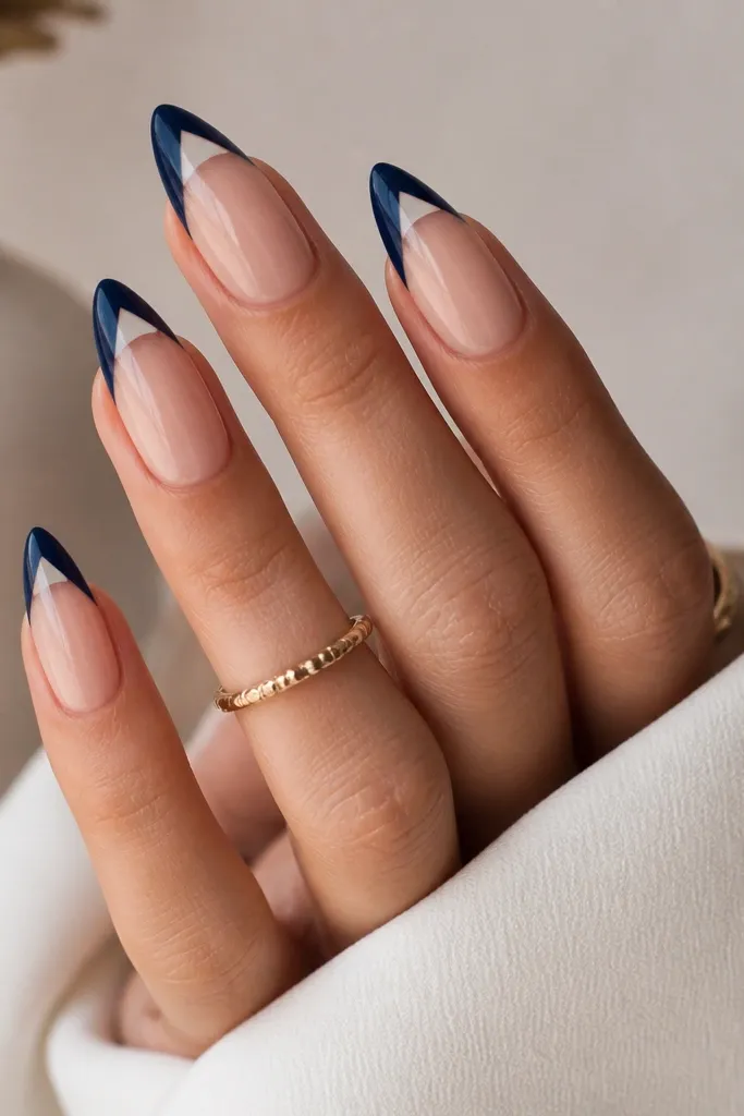 Almond nails with a nude base. The French tip is deep blue, but there's a clear negative space triangle cut out near the center of the tip, leaving a sharp geometric gap. Glossy finish.