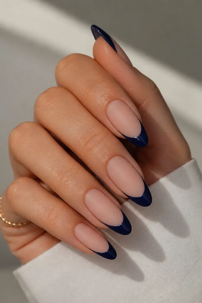 Long almond nails with a nude base. The French tips are navy blue. The nails are matte overall, but there's a thin glossy border right at the tip edge, like a shiny line. The cuticles are clean.