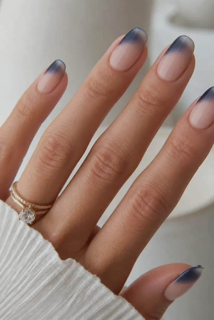 Short to medium nails with a nude base. The French tip starts navy and fades into clear toward the outer edge. The finish is matte over the navy area, with a glossy clear fade at the very tip. Smooth blend, no harsh line.