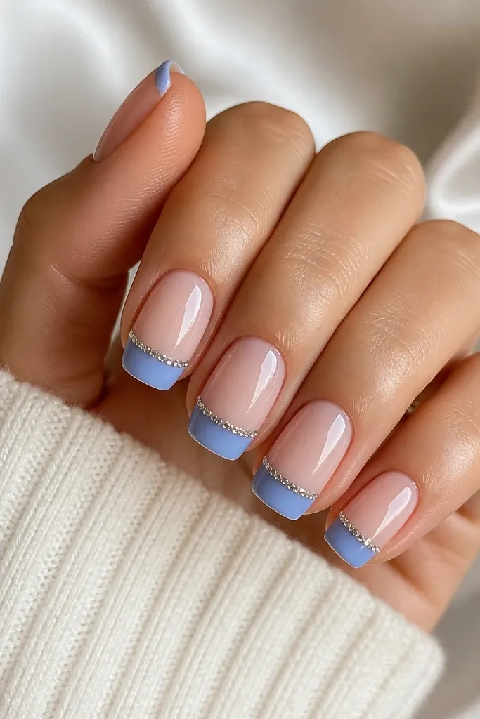 Medium squoval nails with a sheer nude base. French tips are medium blue, glossy. Right on the smile line there is a straight line of micro rhinestones, evenly spaced. Clean cuticles and a polished, sparkly look.