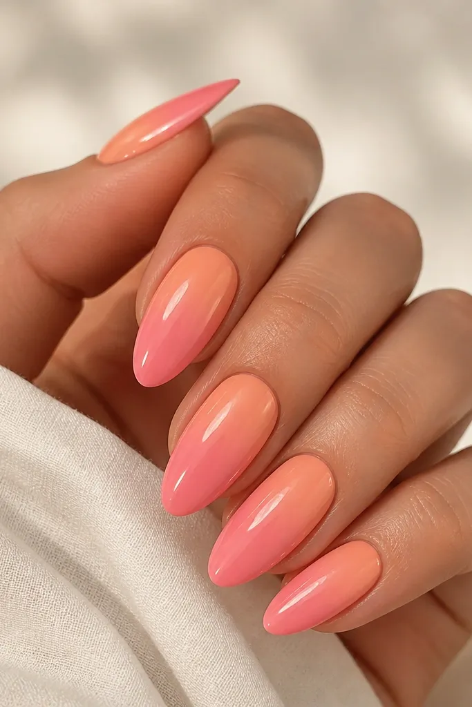 Almond nails with a smooth sunset gradient. The base starts apricot near the cuticle and fades into warm pink toward the tip, with glossy shine and no harsh lines.