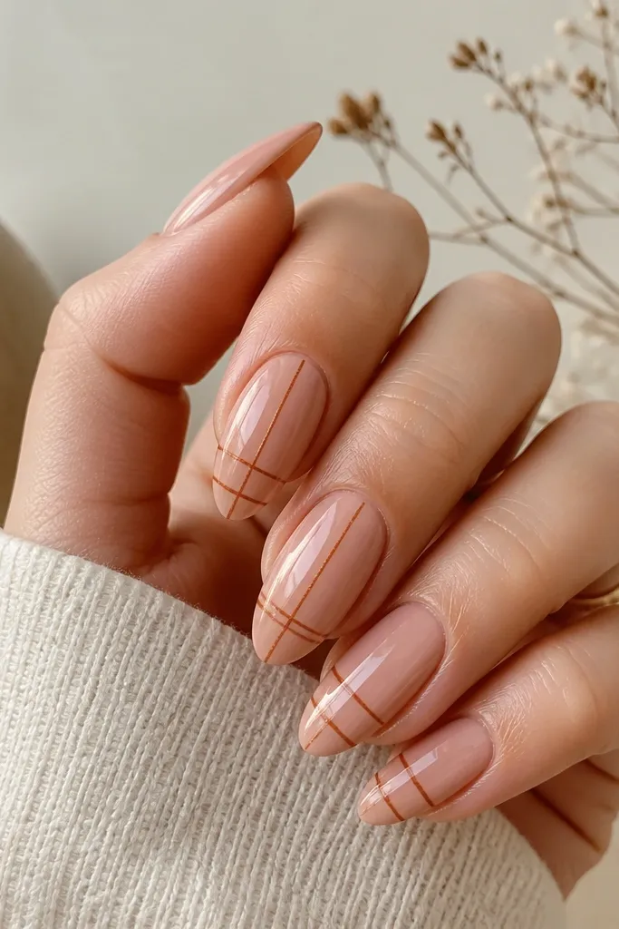 Almond nails painted in a warm nude. Thin terracotta lines form a subtle grid near the center and tip, with a clean, crisp pattern and glossy finish.