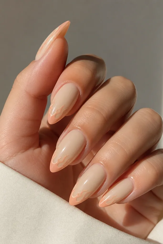 Almond nails in warm beige crème. The tips have tiny flame shapes in peach, like small stylized bursts, outlined softly and filled with peach color, glossy finish.