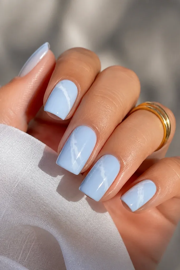 Square nails painted baby blue. Each nail has thin white marble veins that curve diagonally from near the sidewall toward the center, with a glossy finish.