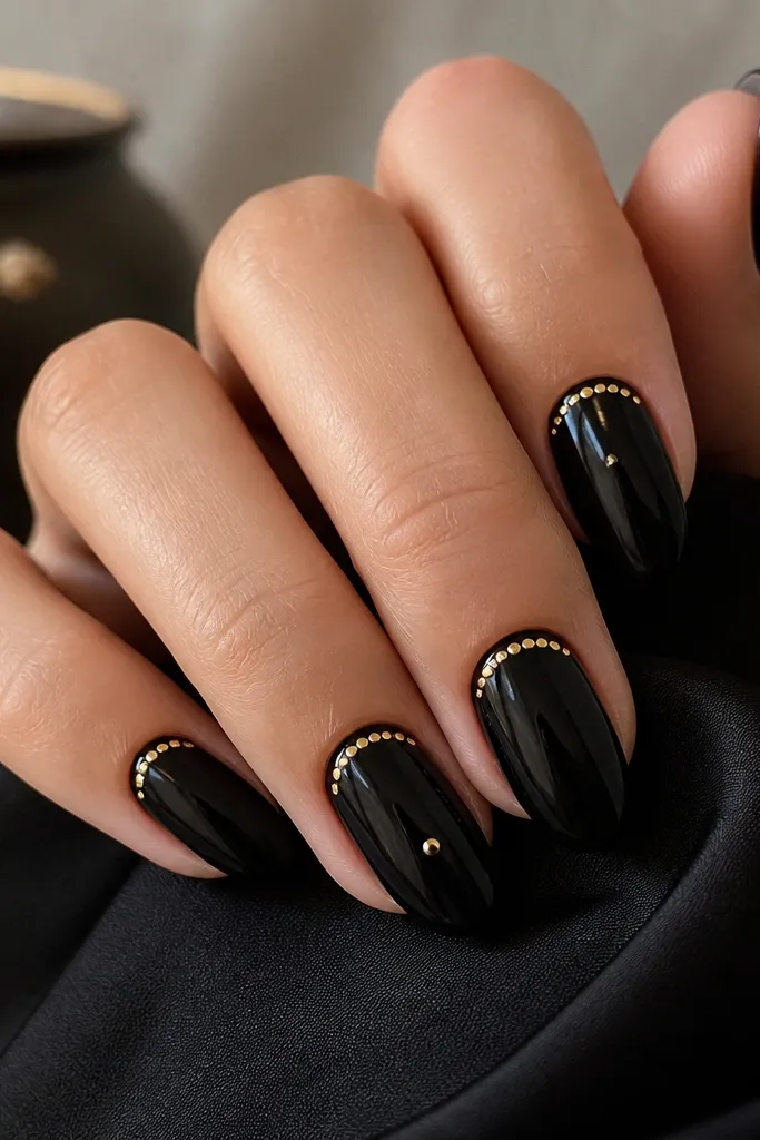 Medium almond nails with glossy black base. A crescent arc made of tiny gold dots sits under the cuticle, and a single gold dot accent appears near the center on two nails.