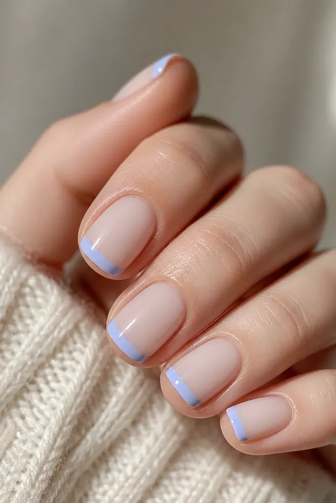 Short square nails with a milky nude base. The tips are a thin band of powder periwinkle blue, crisp and straight across, with a high-gloss finish.