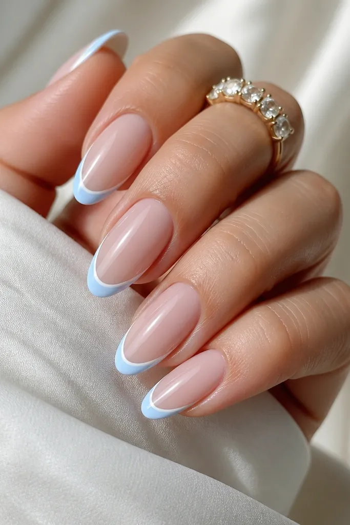 Almond nails with a milky nude base. The French tip is baby blue, and there's a very thin white outline along the very edge of the tip, all glossy.