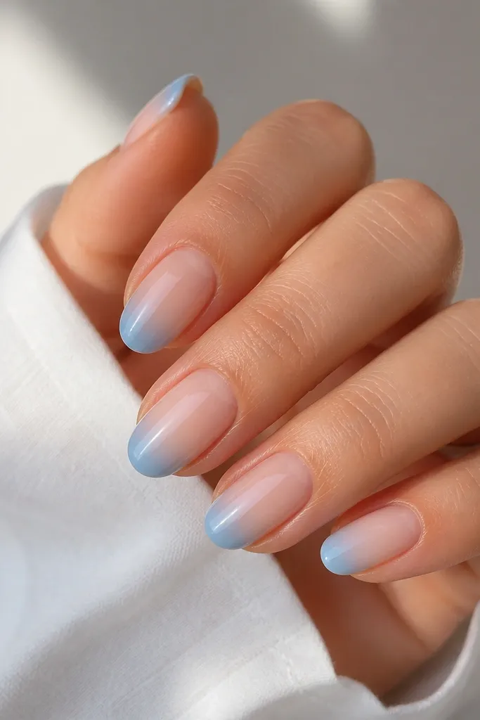Short-to-medium oval nails with a nude base. The tips fade from a deeper light blue near the edge into a lighter misty blue toward the smile line, glossy.