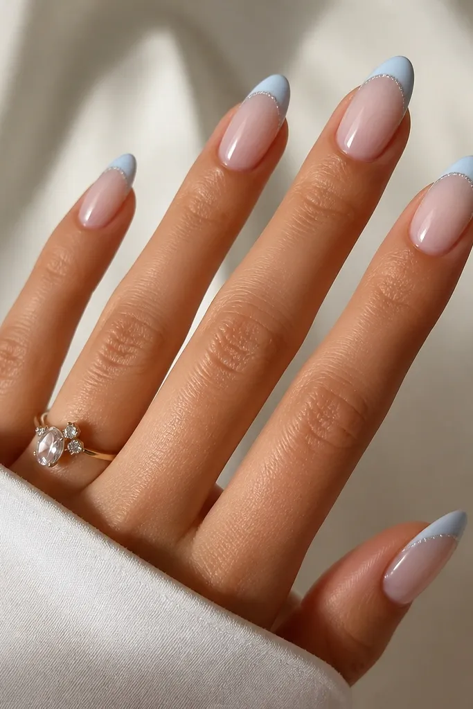Almond nails with a nude base. Light sky blue French tips have a fine glitter line only along the outer edge, like a thin sparkle halo.