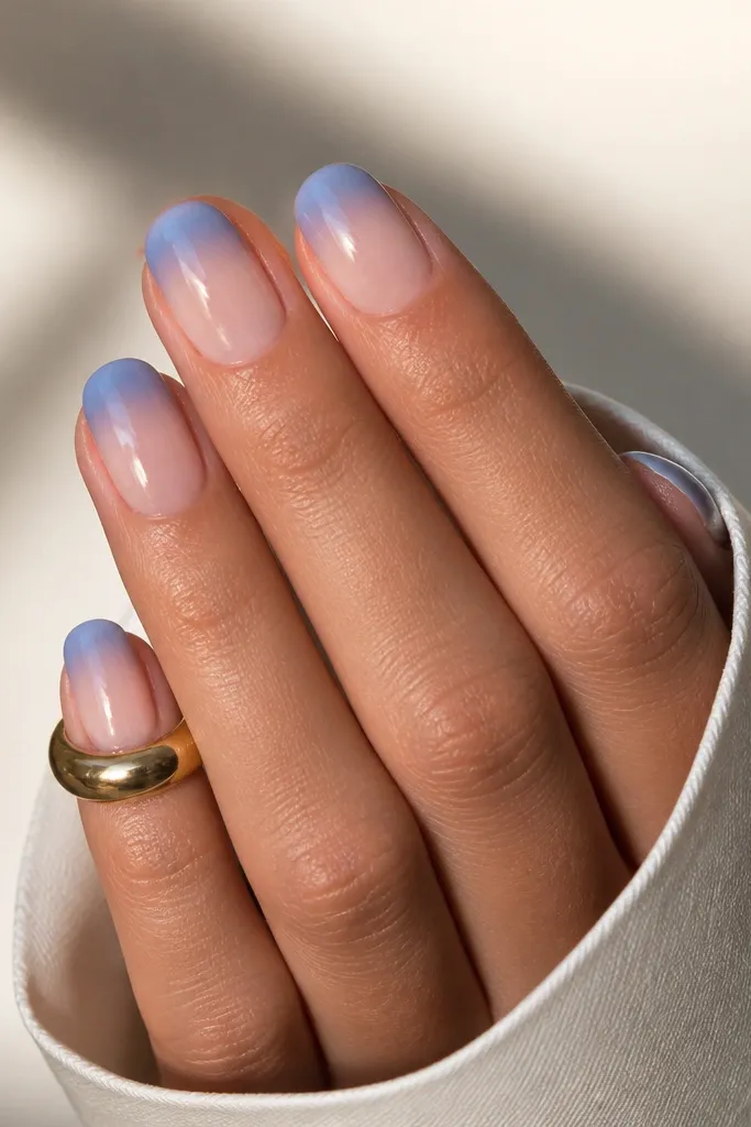 Short oval nails. The tips are cornflower blue, but the top half of the tip looks frosted or semi-opaque, with a smooth gradient to clear nude at the lower edge, glossy.