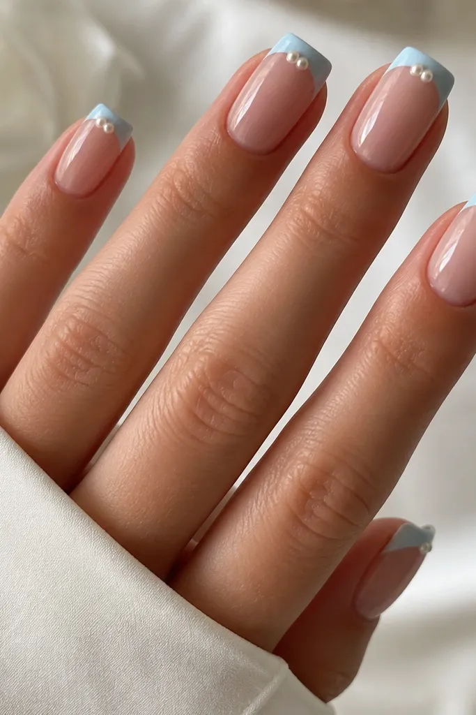 Medium square nails. Milky nude base. Light blue French tips with two tiny pearl beads placed at the center of each tip's top edge, glossy.