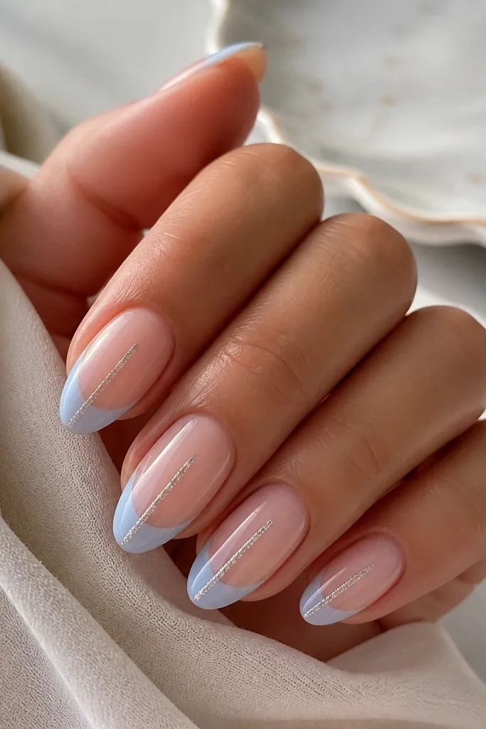 Medium almond nails with nude base. Light blue French tips have a single thin glitter line running vertically up the center from the tip edge, glossy.