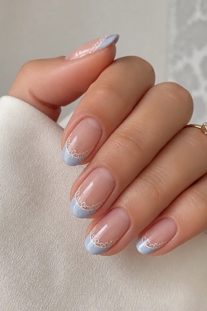 Medium oval nails. Nude base. Light sky blue French tips with delicate white linework that looks like lace, concentrated near the outer edges, glossy.