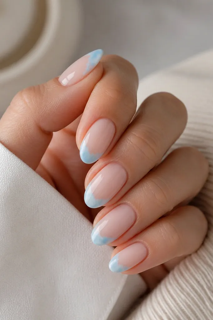 Short almond nails with a nude base. The French tips are light blue, but the top edge looks cloud-soft with a watercolor fade, glossy.