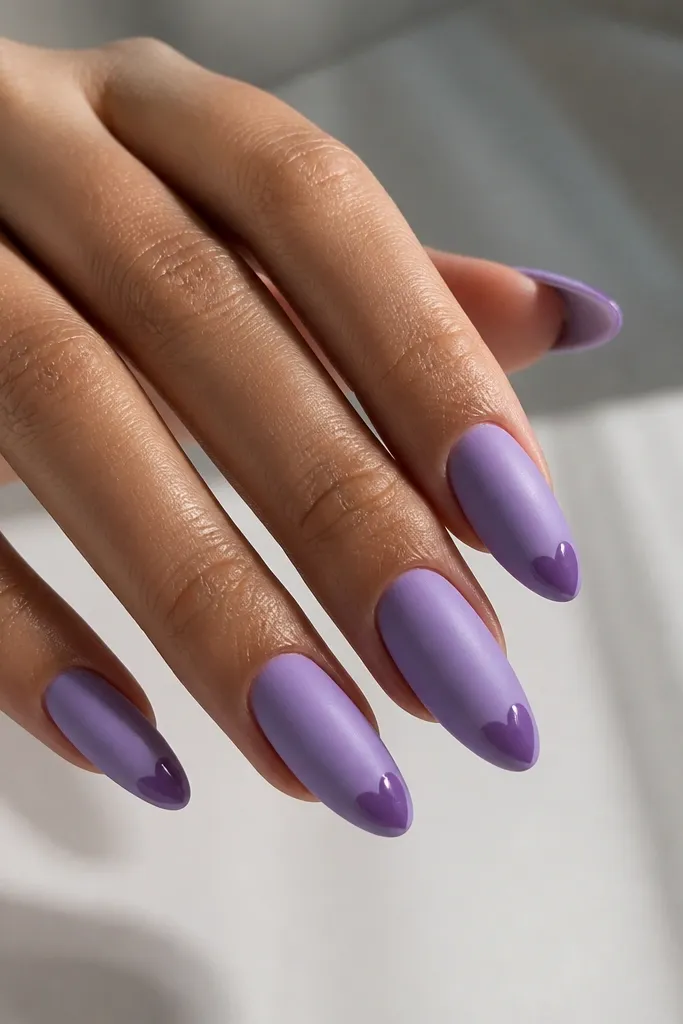 Long almond nails with a lavender satin-matte finish on the whole nail, and glossy heart shapes at the tips in a slightly darker purple; clean cuticle and crisp heart edges.