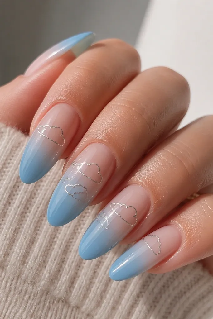 Long almond nails with a sky-blue ombré that fades from sheer near the cuticle to deeper blue at the tip, plus thin silver line art clouds near the cuticle and mid-nail; glossy finish.
