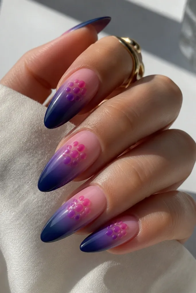 Long almond nails with a deep blueberry to sheer nude gradient, and jelly-like dot clusters in bright pink and purple placed near the center and cuticle; glossy, candy-like finish.